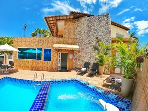 A pool area with a tiled pool, lounge chairs, and a stone wall. - Pousada Sereia do Porto (Ipojuca)