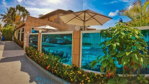 A modern building with a pool area, surrounded by tropical plants and a clear blue sky. - Pousada Sereia do Porto (Ipojuca)