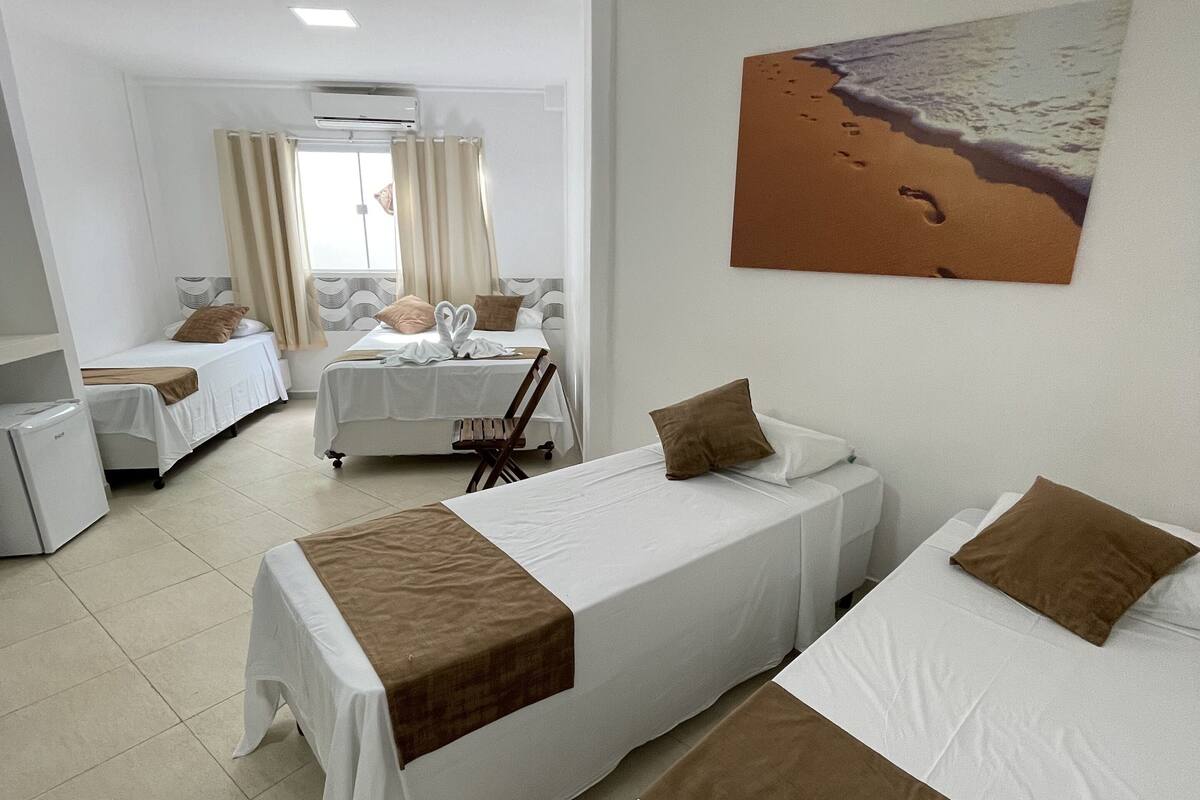 A hotel room with two beds, a small desk, a chair, and a painting of a beach.
