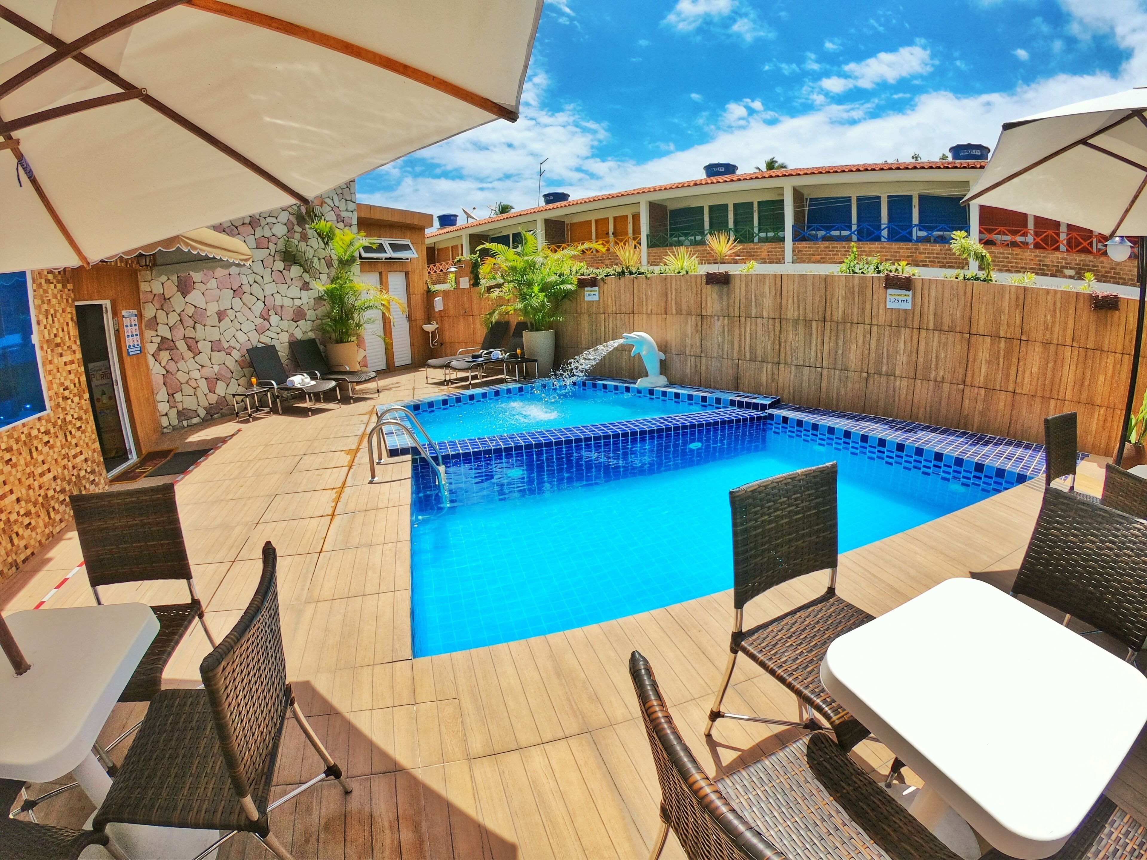 Una piscina con borde de azulejos, rodeada de una terraza de madera y muebles de mimbre.
