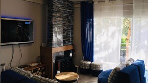A living room with a stone fireplace, a television, a sofa, and a window with curtains.