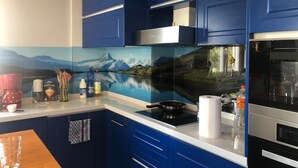 A modern kitchen with blue cabinets, a stove, and a large window overlooking a scenic mountain landscape.