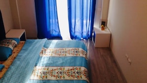 A bedroom with a bed, blue curtains, a small bedside table, and a nightstand.