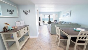 A living room with a view of the ocean, a dining area with a table and chairs, and a kitchenette with a counter and shelves. - August 2026 Big Savings!!! Remodeled bathrooms! BEACHFRONT (St. George Island)