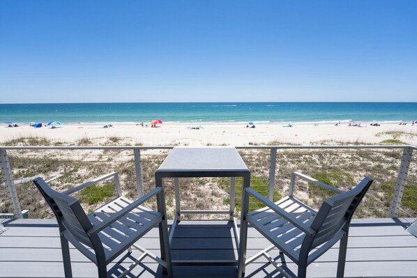 Eine Terrasse mit Tisch und Stühlen mit Blick auf einen Strand.