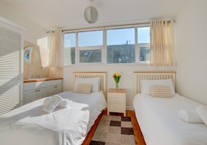 Two single beds with white linens and matching pillows, a bedside table, and a large window with curtains.