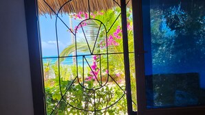 Una ventana con vista a un jardín tropical y el océano.
