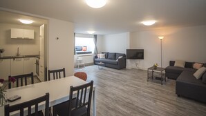 A modern living room with a sofa, a dining table with chairs, a kitchen area with cabinets, and a TV mounted on the wall. - Bad Zandvoort 4: Cosy & Modern Apartment in the basement, close to the sea (Zandvoort)
