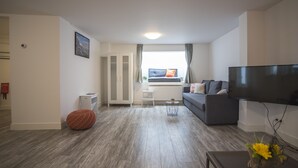 A modern living room with a grey sofa, a flat-screen TV, and a wooden floor. - Bad Zandvoort 4: Cosy & Modern Apartment in the basement, close to the sea (Zandvoort)