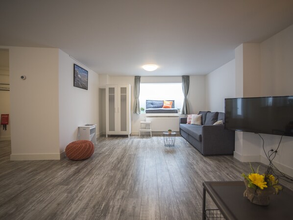A modern living room with a grey sofa, a flat-screen TV, and a wooden floor.