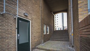 A narrow brick alleyway with a green door, a small window, and a set of stairs leading to a higher level. - Bad Zandvoort 4: Cosy & Modern Apartment in the basement, close to the sea (Zandvoort)
