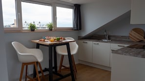 A modern kitchen with a dining table, two white chairs, a window with a view of buildings, and a wooden countertop.