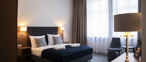 A modern hotel room with a large bed, bedside lamps, a desk, and a chair.
