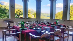A dining area with a table set for a meal, large arched windows, and a view of a mountainous landscape. - Vanatun Monastery Stay (Dilijan)