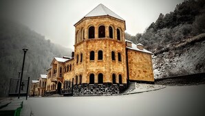 A historic stone building with a central tower and arched windows, surrounded by a snowy landscape. - Vanatun Monastery Stay (Dilijan)