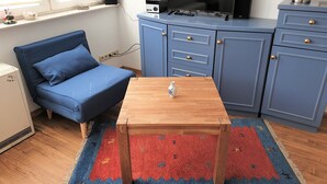 Un espace de vie compact avec un canapé bleu, une table en bois, un téléviseur posé sur un meuble et un tapis à motifs.