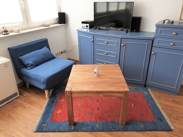 A compact living space with a blue sofa, a wooden table, a TV on a cabinet, and a patterned rug.
