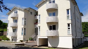 Un immeuble résidentiel à plusieurs étages, doté de balcons, d’un escalier central et d’un petit jardin à l’avant.