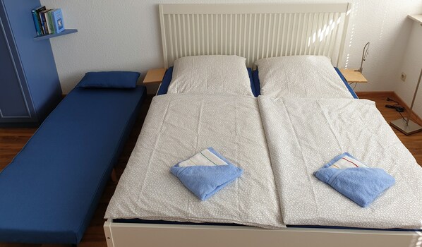 A twin bed with a patterned bedspread, a blue pillow, and a matching blue pillow on the footboard.