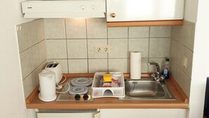 Une petite cuisine équipée avec des meubles blancs, un four encastré, un évier et un plan de travail sur lequel se trouvent un grille-pain, des assiettes et un égouttoir.