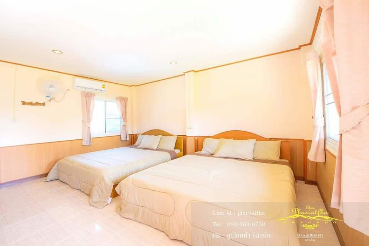 A hotel room with two beds, a window with curtains, an air conditioning unit, and a wooden headboard.