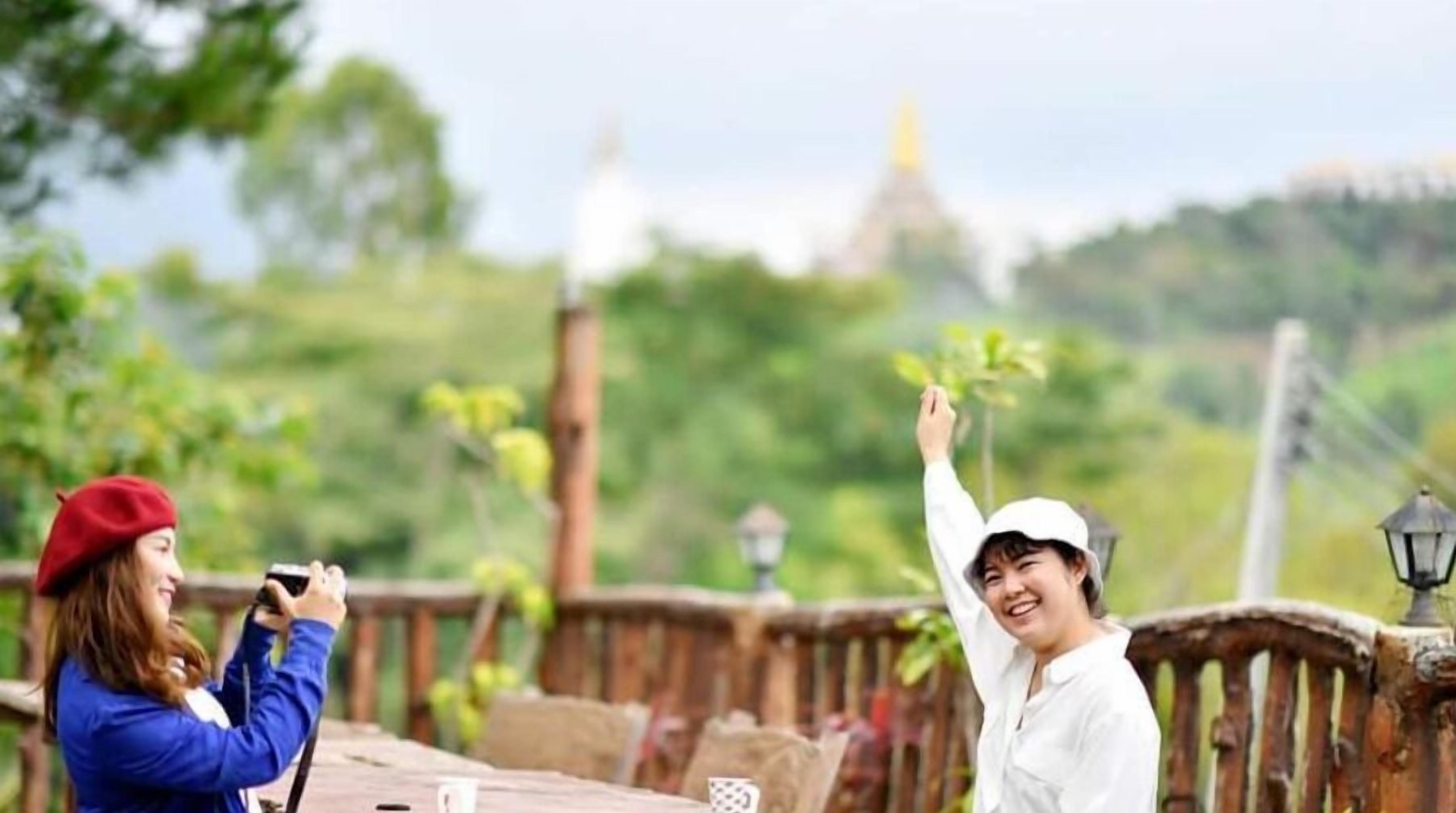 Two people on a bridge with a view of a temple and greenery in the background.