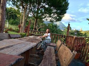 A person sitting on a wooden bench in an outdoor setting with a view of a mountain and temple in the background. - Phusiatfha Resort (Khao Kho)