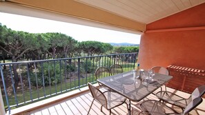 Un balcon avec une table et des chaises, donnant sur des arbres et un paysage lointain.