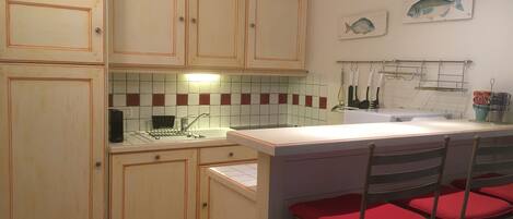 A kitchen with wooden cabinets, a tiled backsplash, a sink, and a bar area with red cushioned stools.