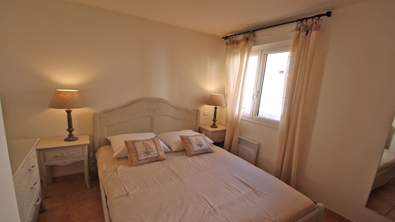 Un dormitorio con una cama individual, dos mesitas de noche con lámparas, una ventana con cortinas y un aparador con cajones.