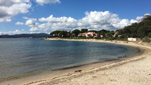Una playa con agua cristalina, orilla de arena y casas al fondo.