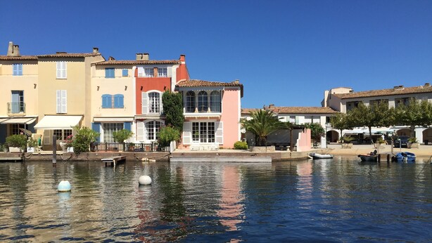 Una propiedad frente al agua con un canal, que cuenta con edificios con balcones y un cielo azul despejado.