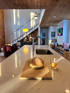 A modern kitchen with a marble countertop, a loaf of bread, and a glass of drink.