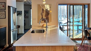 Una cocina moderna con techo de madera, una isla grande con un fregadero y vistas a una terraza exterior nevada.