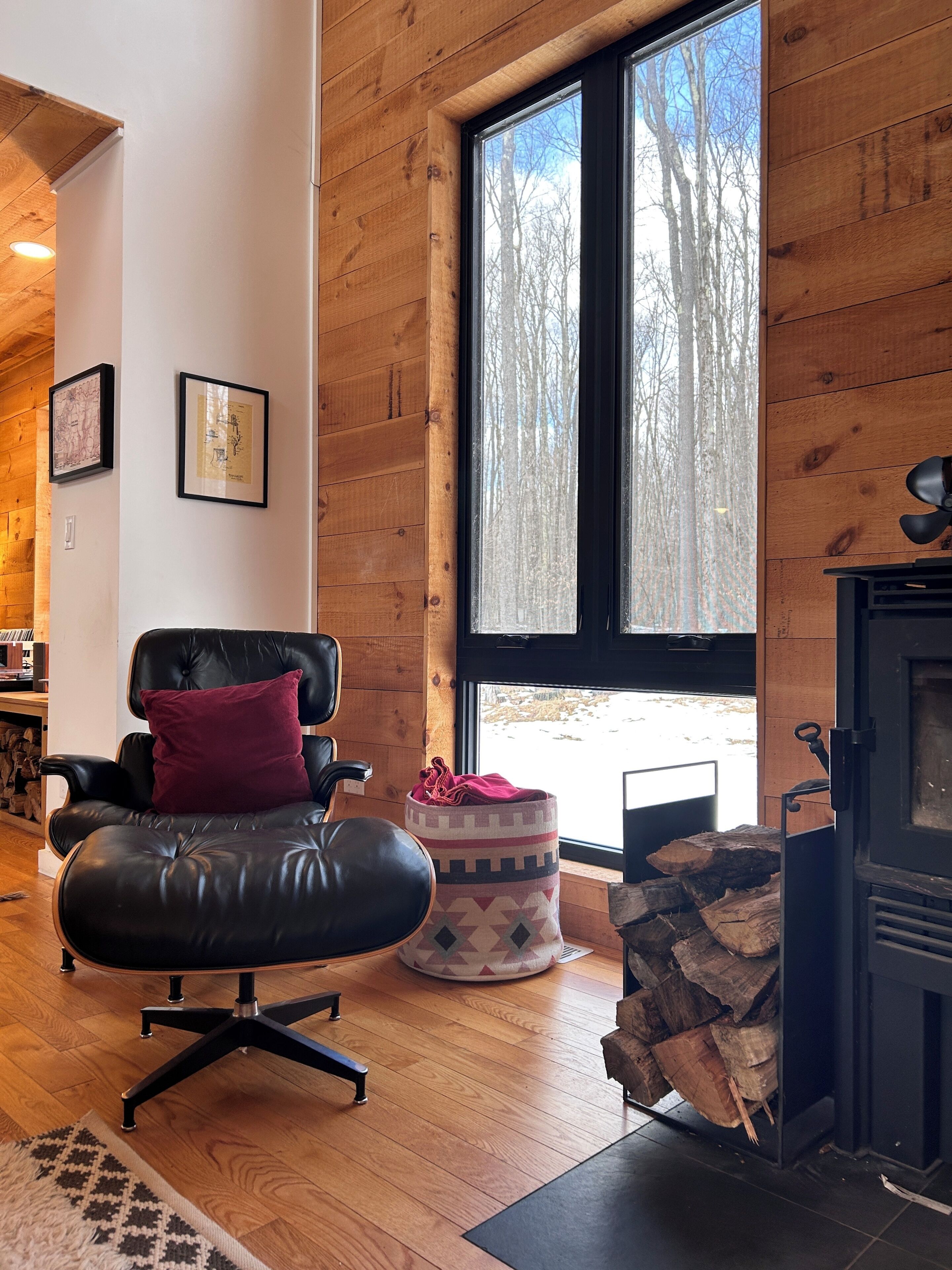 A cozy room with a leather chair, a small ottoman, a fireplace, and a large window with a view of trees.