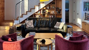 Un amplio salón con una escalera, un sofá de cuero, una mesa de centro y una estantería.