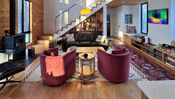 Amplia sala de estar con techo de madera, escalera, chimenea y televisor grande.