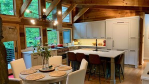 Een moderne keuken met houten balken, een centraal eiland, witte kastjes, en een eethoek met een ronde tafel en stoelen.