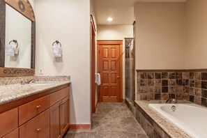 A bathroom with a large mirror, wooden vanity, granite countertop, and a bathtub with a tiled shower area. - Timbers #1031 (Mammoth Lakes)