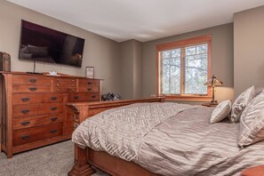 A bedroom with a large bed, wooden dresser, and a television mounted on the wall. - Timbers #1031 (Mammoth Lakes)