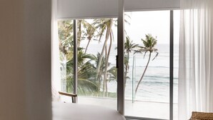 Ein Zimmer mit einer großen Schiebeglasdoor zum Balkon mit Blick auf Palmen und das Meer.