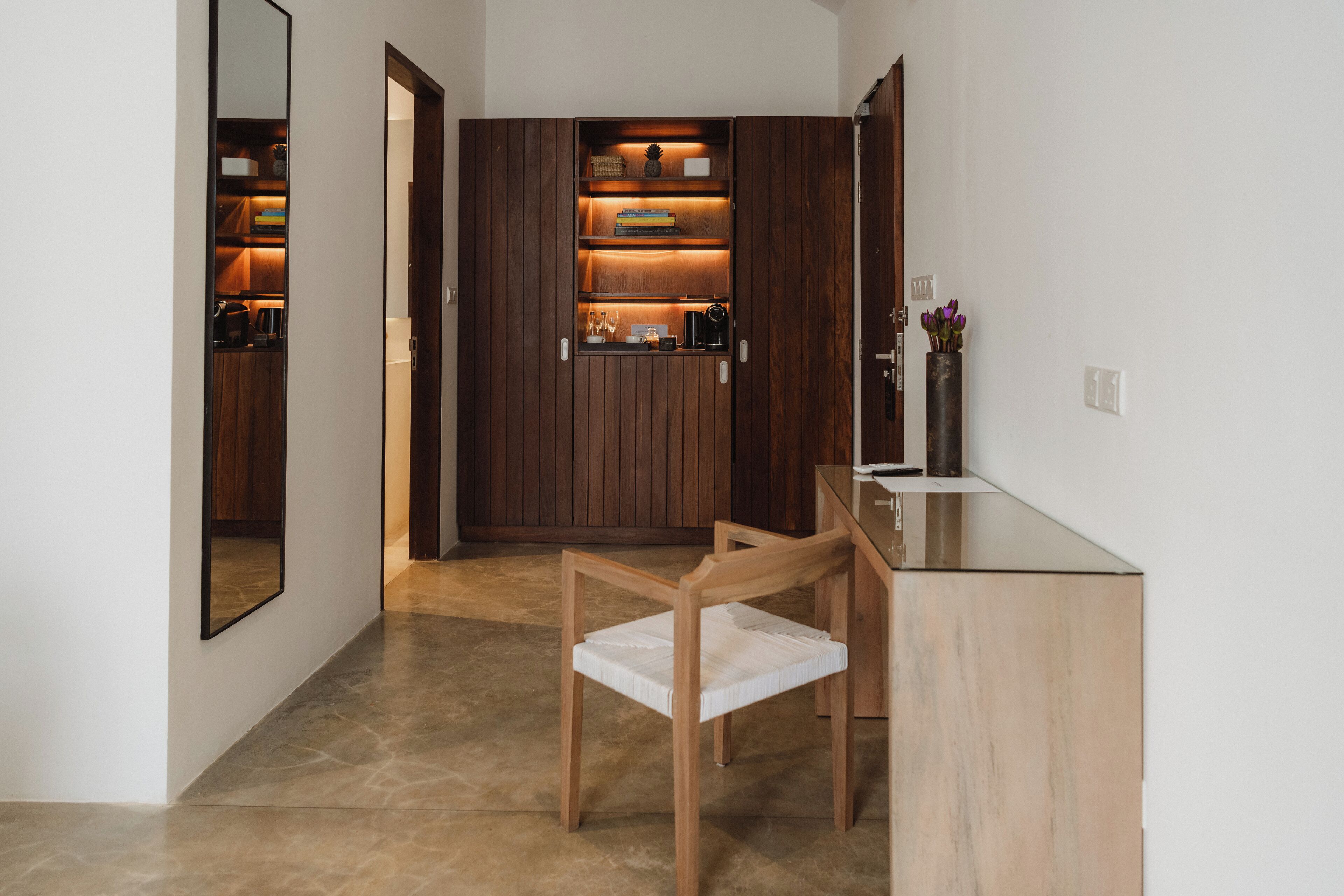 Un couloir avec une armoire en bois, une chaise et une petite table sur laquelle se trouve un vase.