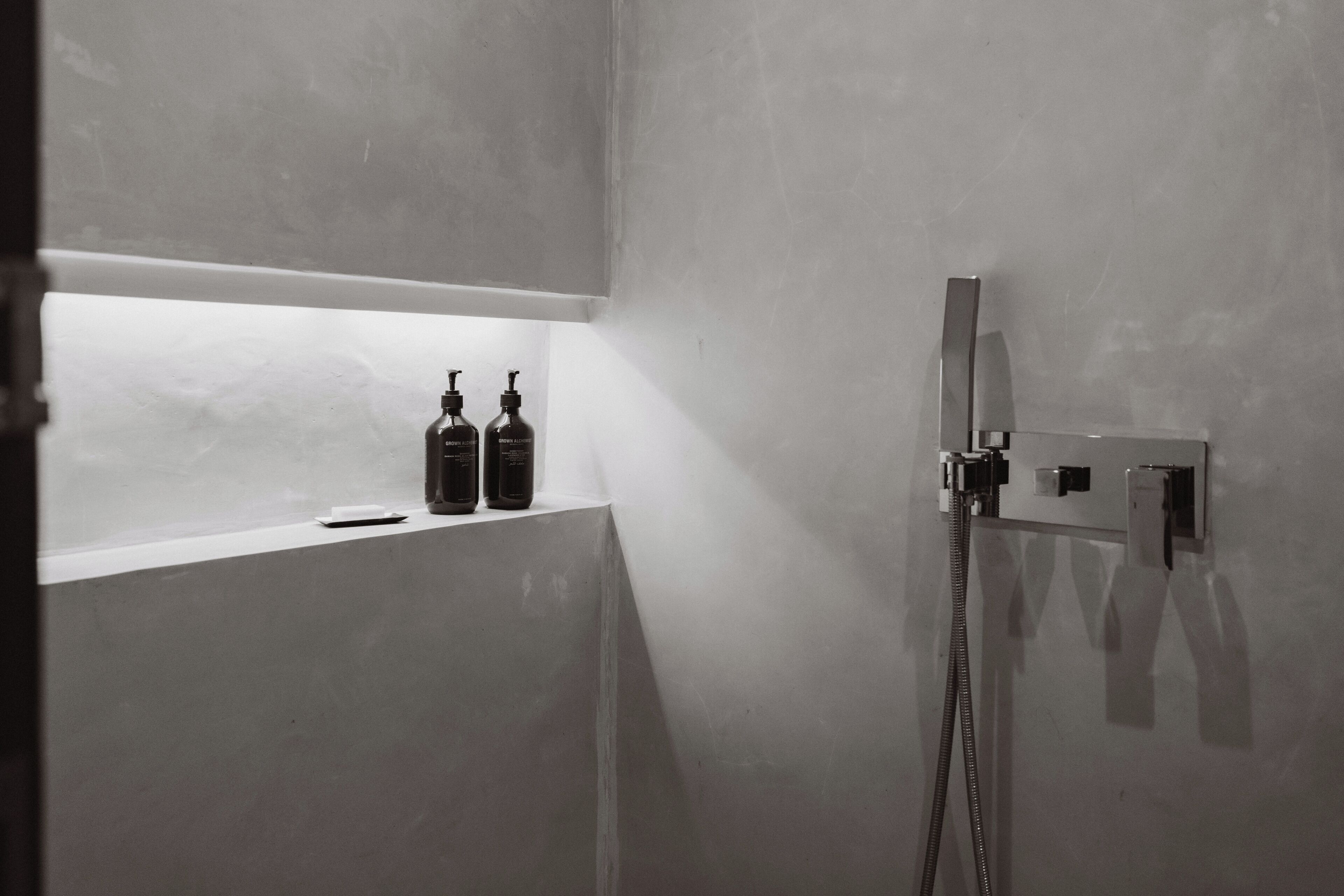 A bathroom with a shower, a shelf with two bottles, and a mirror.