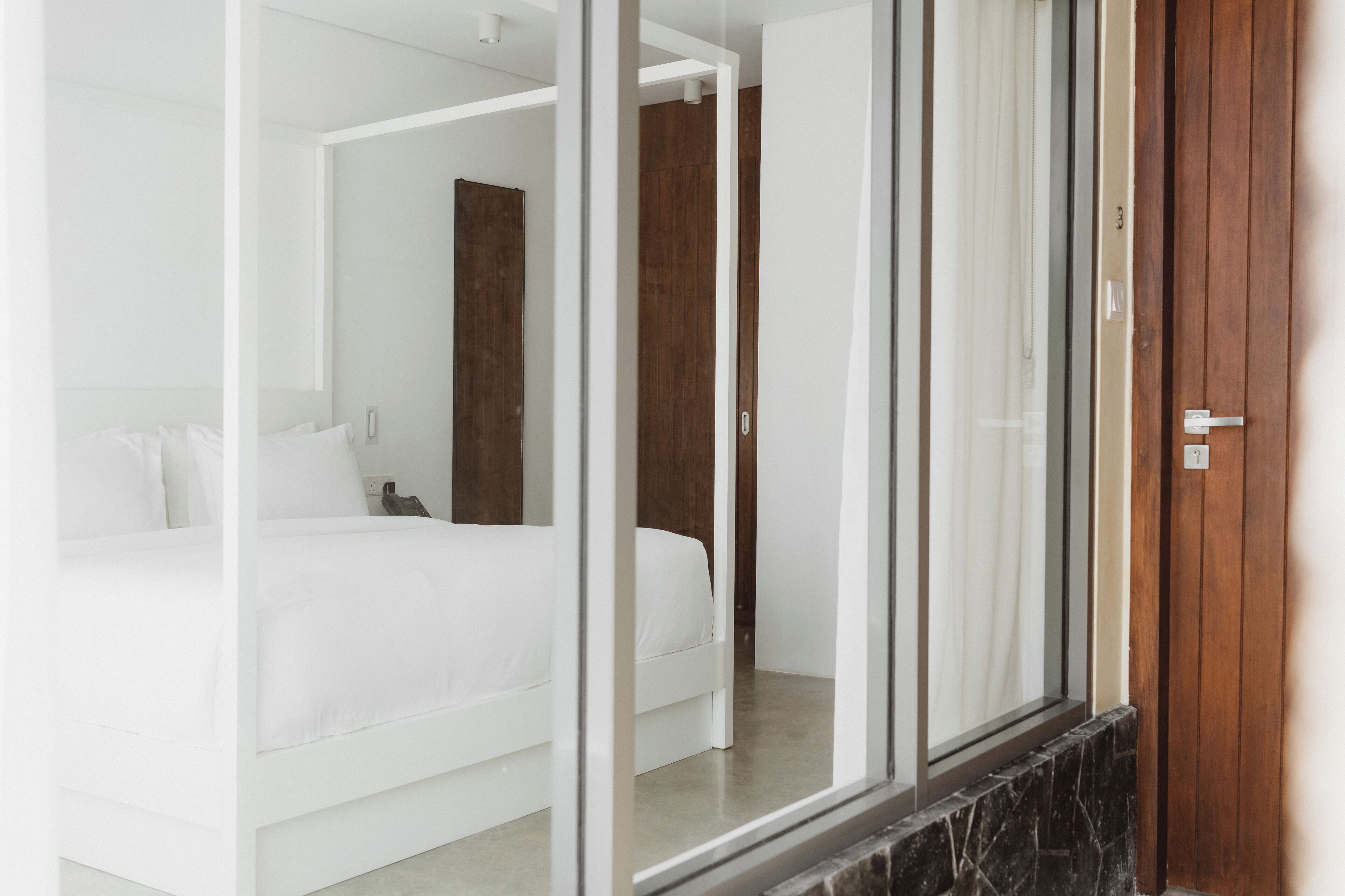 Una camera d'albergo moderna con un letto grande, una porta in legno e un divisorio in vetro.