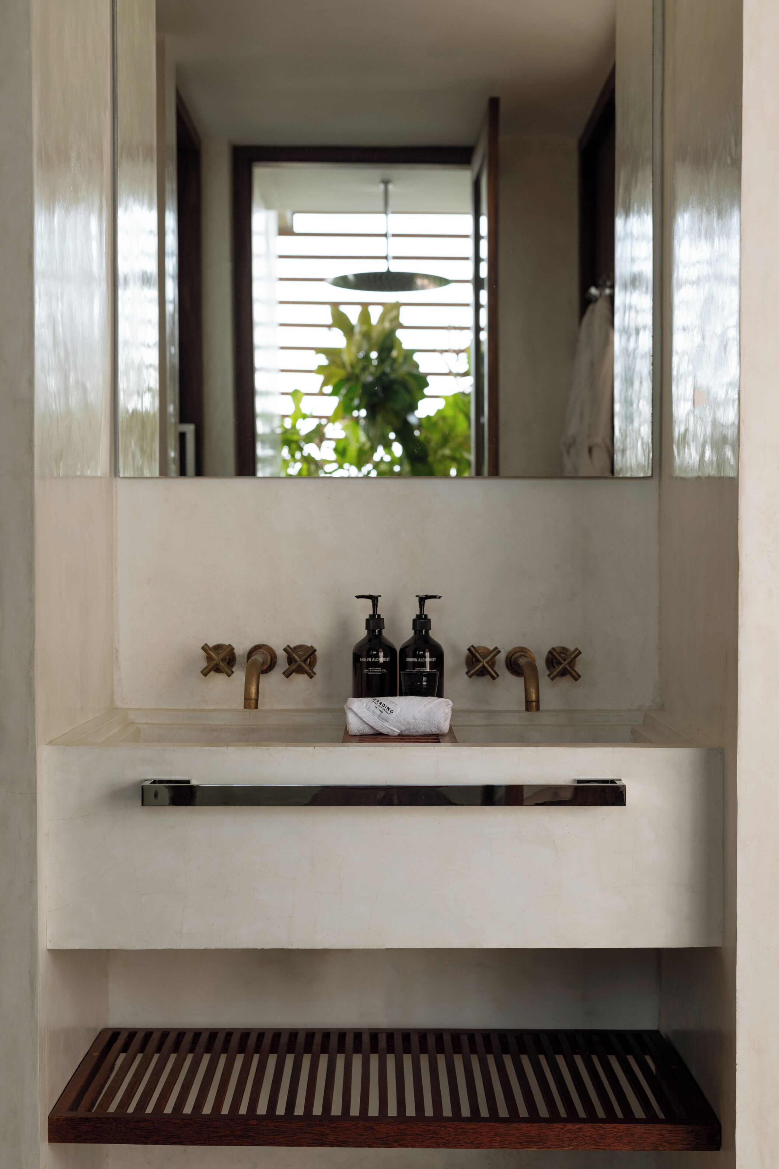 Un bagno con un lavandino bianco, due rubinetti, uno specchio e una mensola in legno sotto.