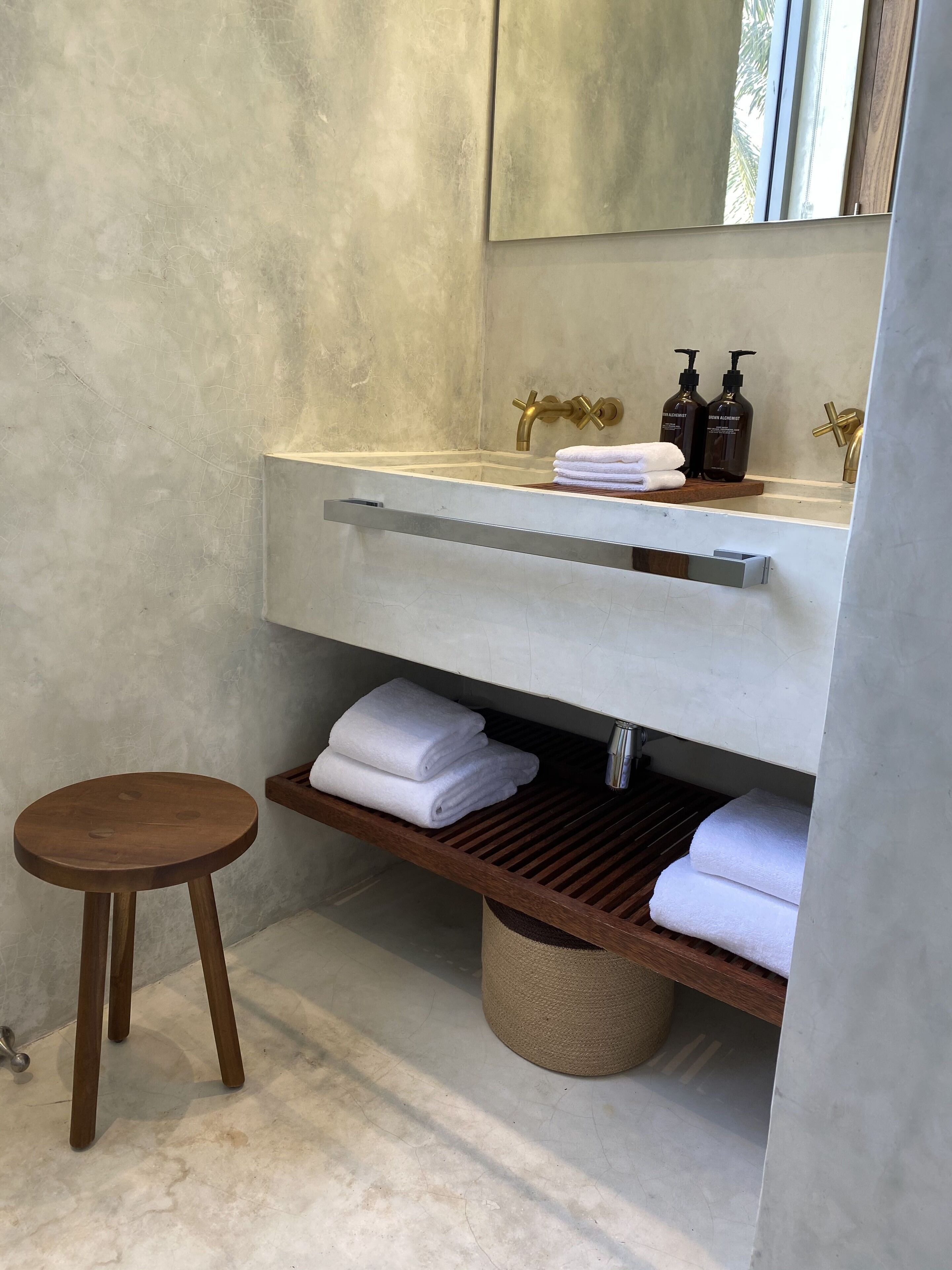 A bathroom with a marble sink, gold faucets, and a wooden stool.