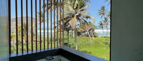 A bathroom with a bathtub, a window with a view of palm trees and the ocean, and a wooden railing.