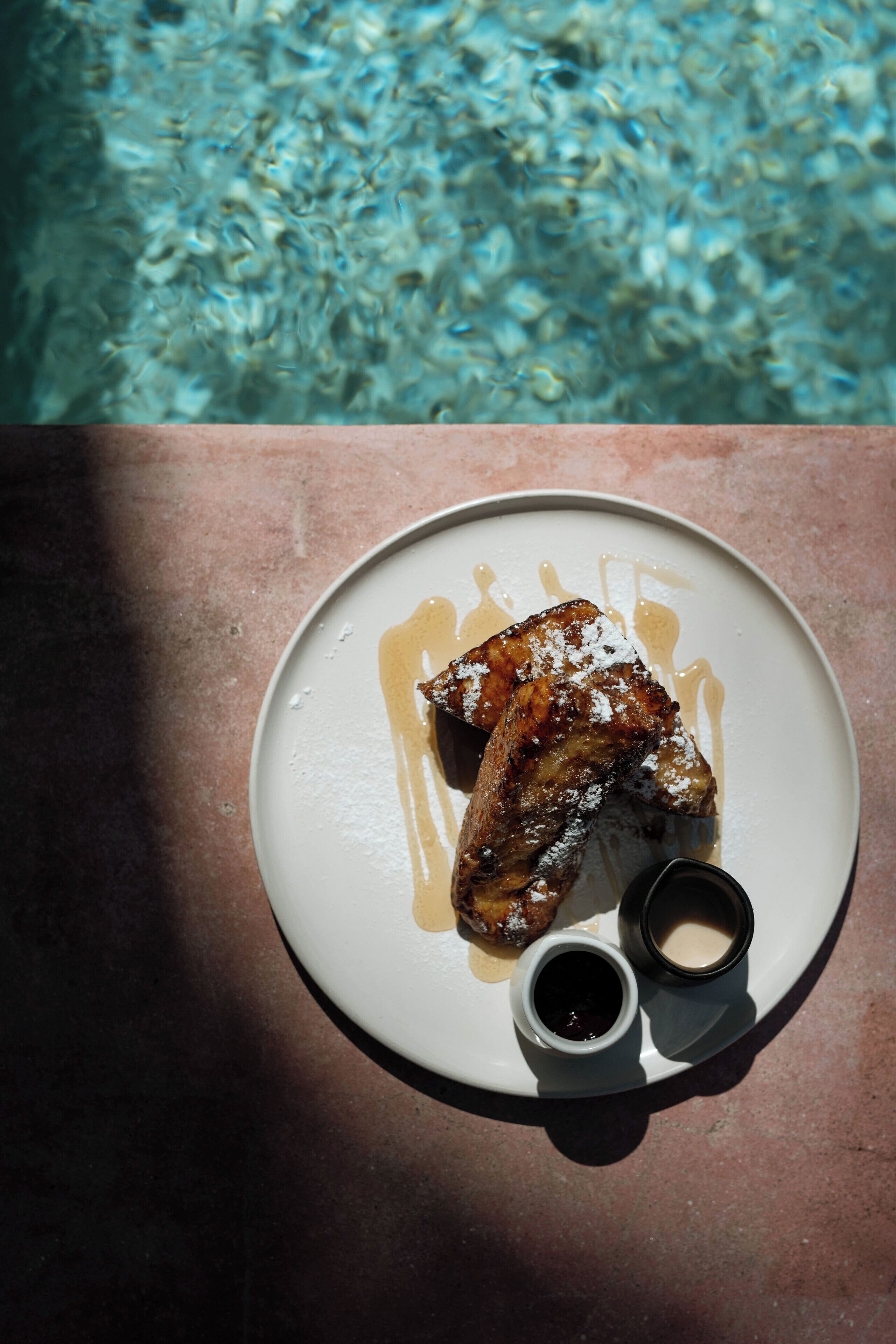 Un plato con comida y dos tazas pequeñas sobre una mesa junto a una piscina.
