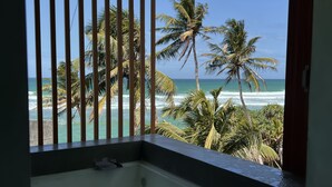 Ein Badezimmer mit einer Badewanne, einem Fenster mit vertikalen Streben und Blick auf das Meer und Palmen.