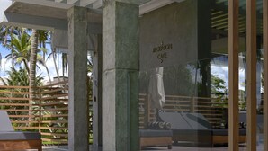 Ein Poolbereich mit Rezeption, Café, Betonsäulen und Holzzaun.